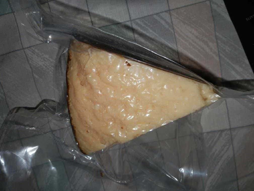 Fetta di torta al formaggio sigillata in pellicola trasparente, pronta per essere conservata o trasportata.