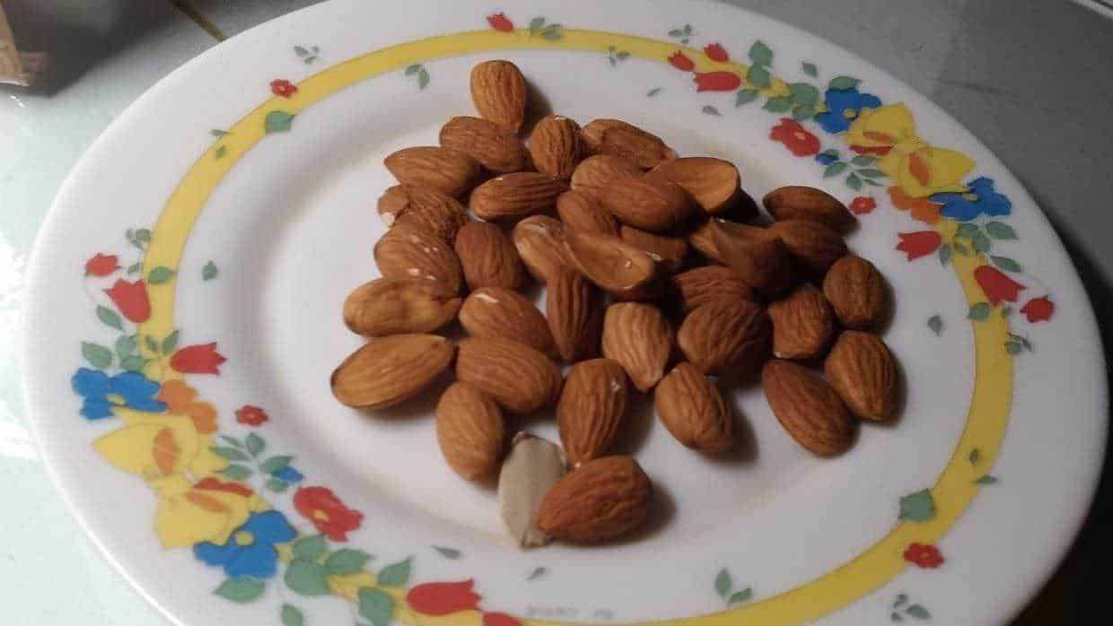 Mandorle tostate crude su piatto decorato con fiori colorati, alimenti naturali, snack salutare, alimentazione sana, aperitivo, ricetta, alimenti biologici, distribuzione alimentare.