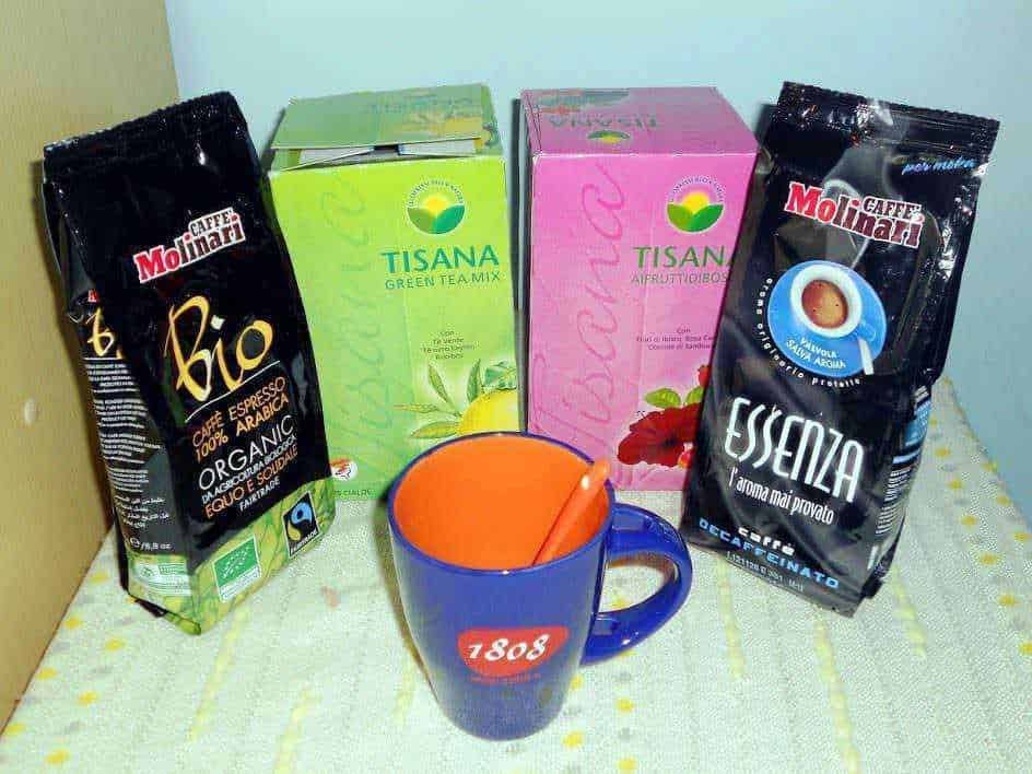 Tè verde e tisane in scatola con caffè biologico in confezioni colorate, tazza da tè blu con cucchiaino arancione.