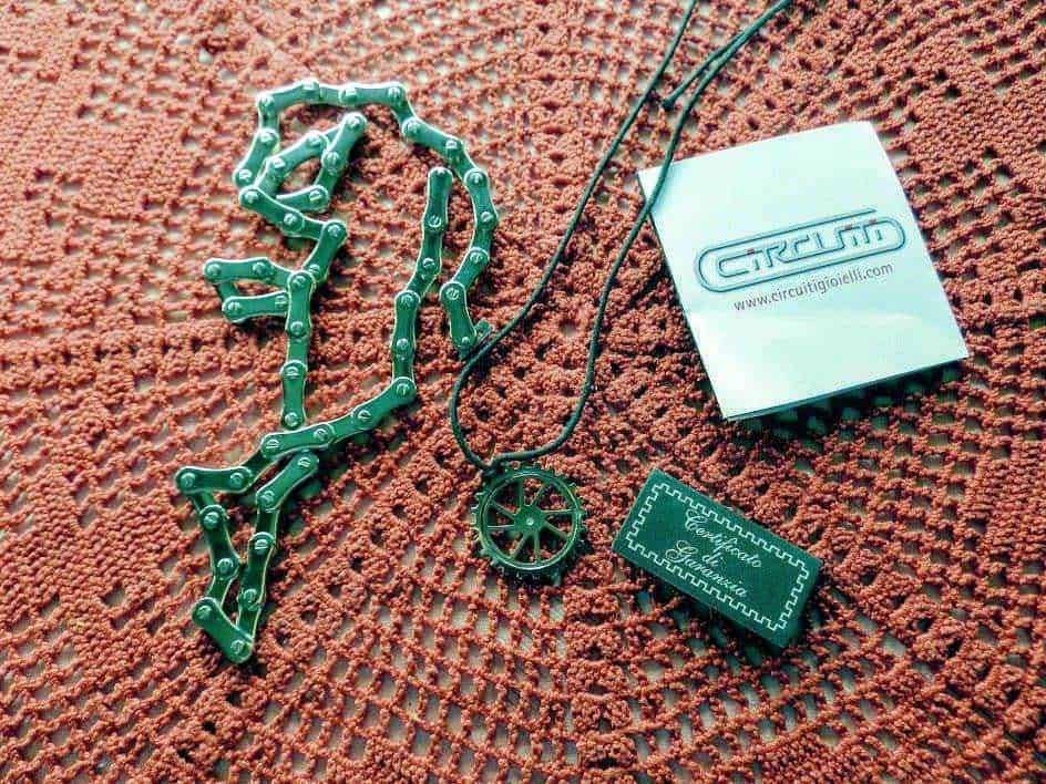 Catenella verde, pendente con medaglia, biglietto da visita Circuiting, su sfondo tessuto rosso.