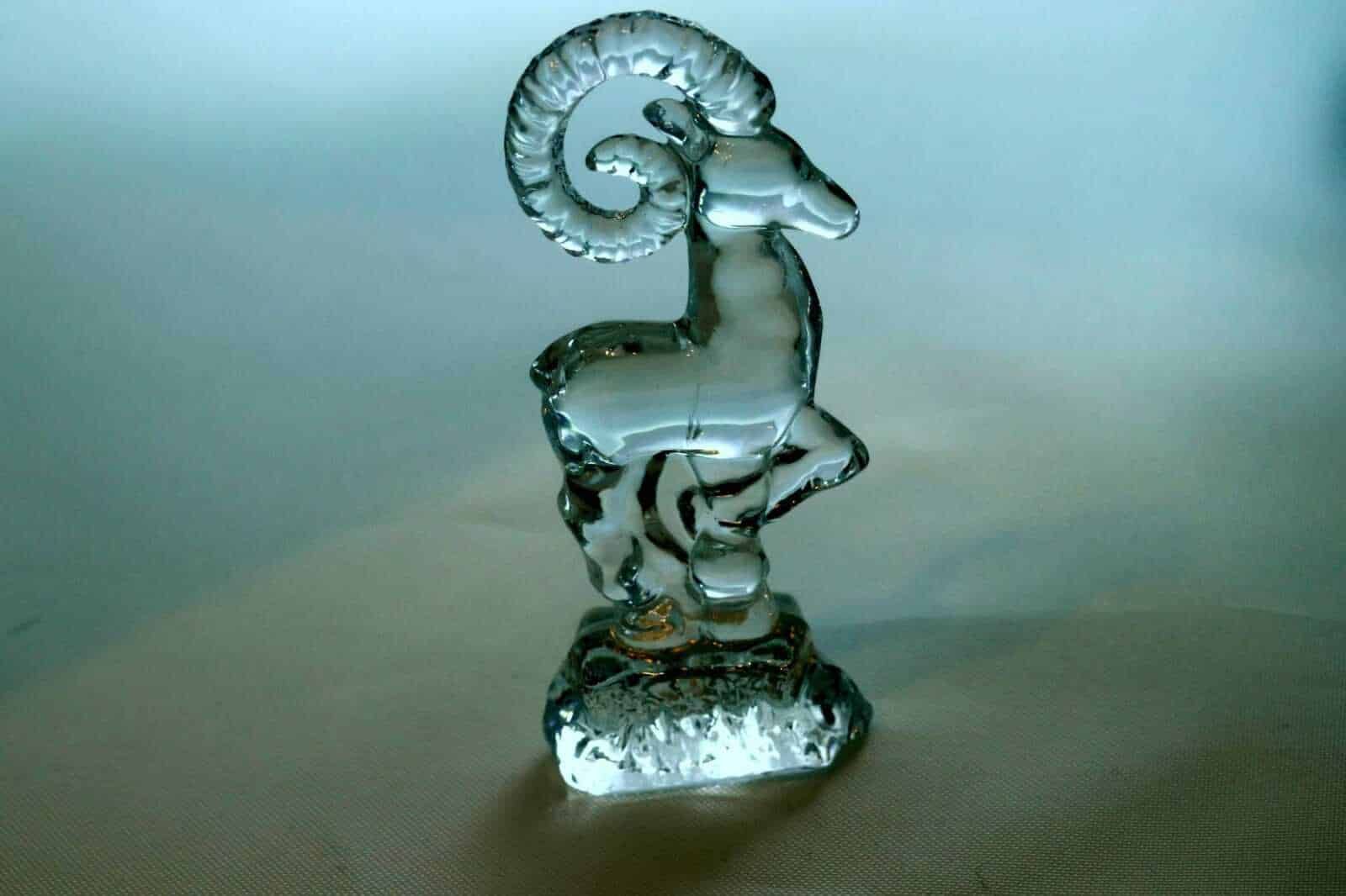 Riflesso di una scultura in vetro a forma di capra con corna arcuate e dettagli trasparenti, simbolo artistico in vetro decorativo.