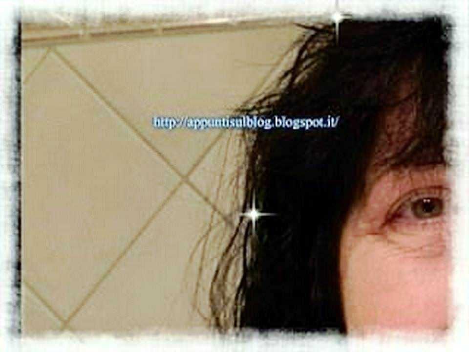 Lunghi capelli neri e volto sorridente, primo piano di una donna con sfondo di piastrelle beige. Immagine brillante e coinvolgente per blog o articoli di lifestyle e bellezza.