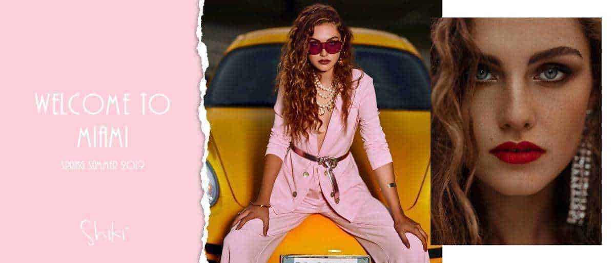 Una donna di stile in abiti rosa seduta su un'auto gialla, con trucco audace e occhiali rosso scuro, raffigurata in un contesto di moda e lifestyle.