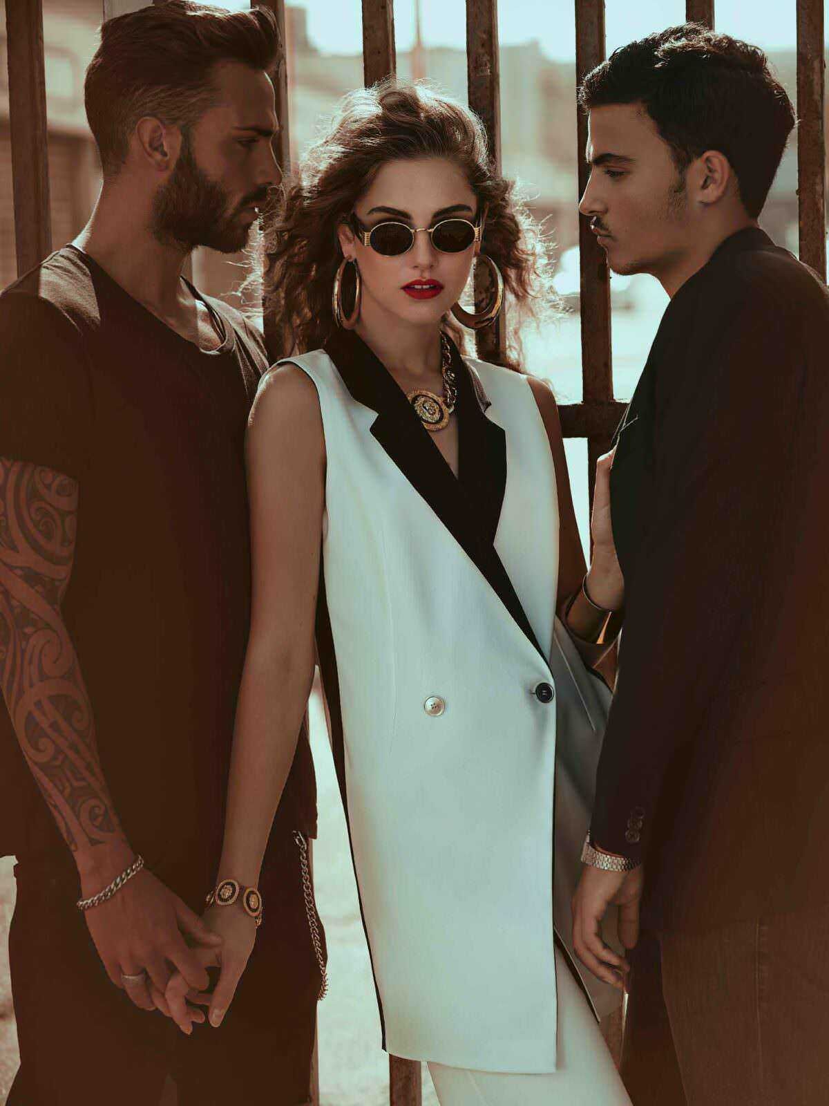 Vestiti alla moda di tre giovani adulti in posa su uno sfondo urbano, con stile unico e accessori di tendenza, evidenziando moda street style e outfit sofisticati.