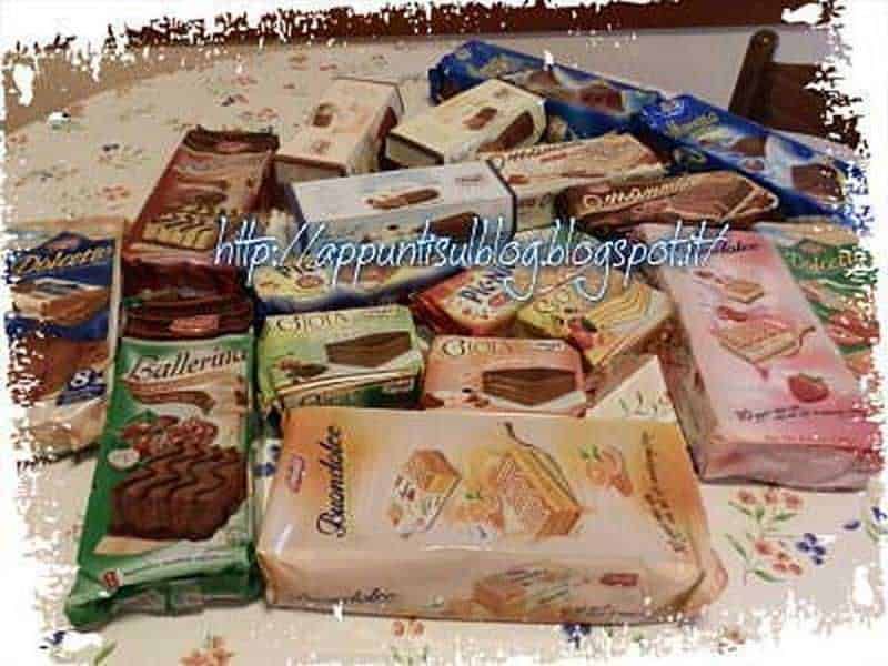 Pacchetti di biscotti e snack dolci assortiti, vari marchi e gusti, su tavolo con tovaglia floreale, snack snackumi e dolciumi, ideale per merende e pause golose.