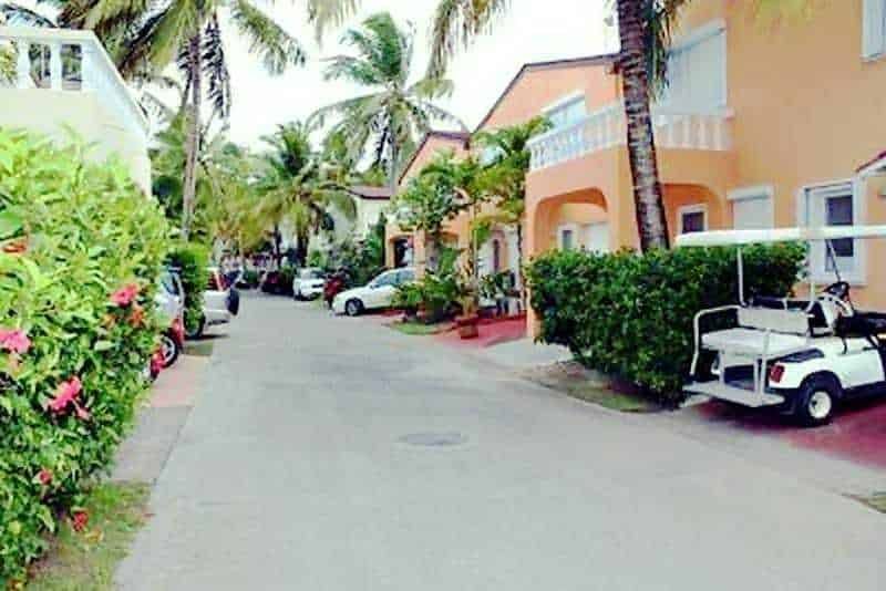 Colorato quartiere residenziale con palme, case color pastello e auto sportive lungo una strada tranquilla, perfetto per vacanze rilassanti e soggiorni al mare.