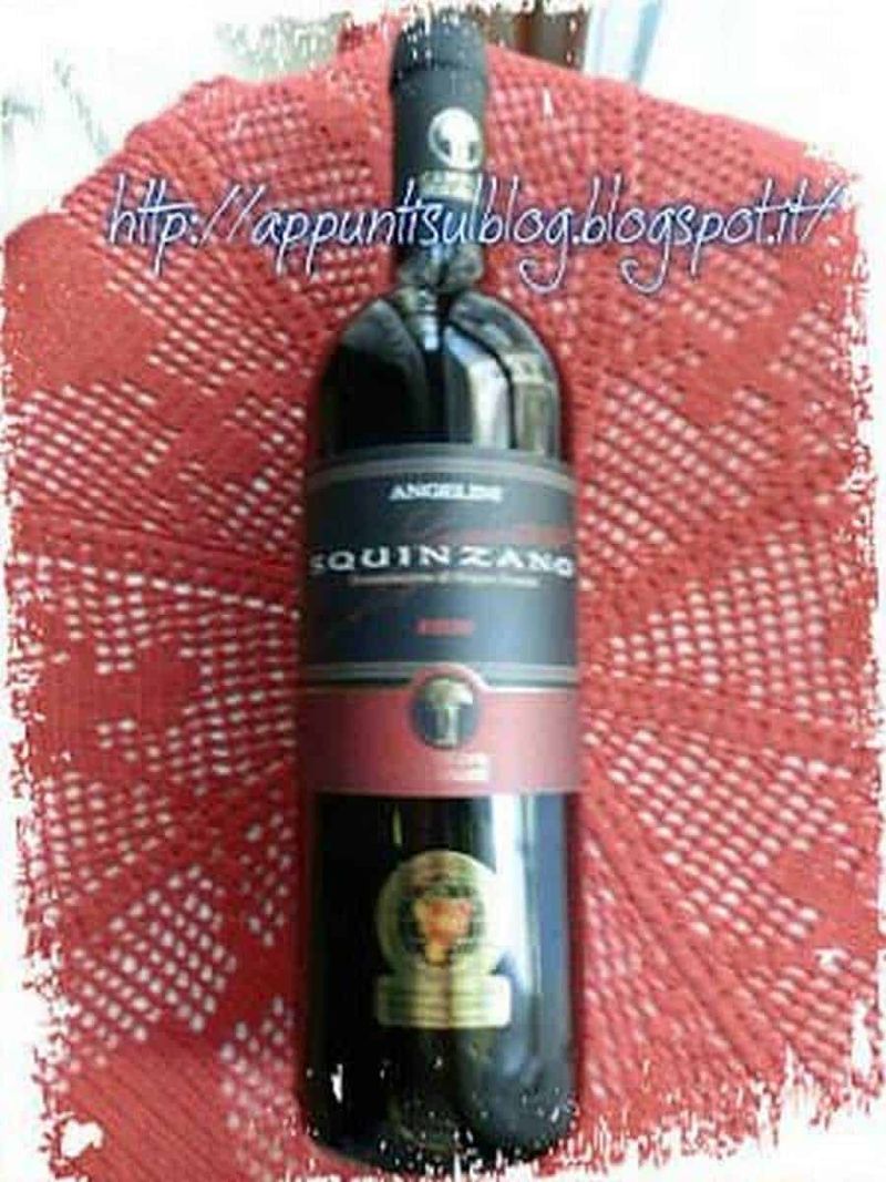 Cantine 2 Palme, vini di qualità fruttati dal sapore delicato 3 Bottiglia di vino rosso con etichetta "Squinzano" su sfondo di tovaglia rossa a rete.