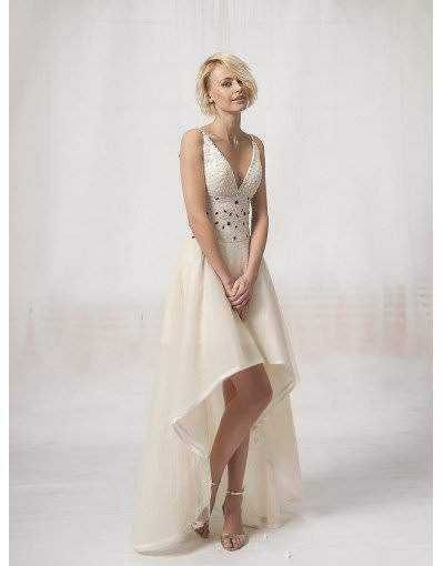 Elegante donna in abito da sera bianco con gonna lunga e dettagli in pizzo, posa su sfondo neutro.