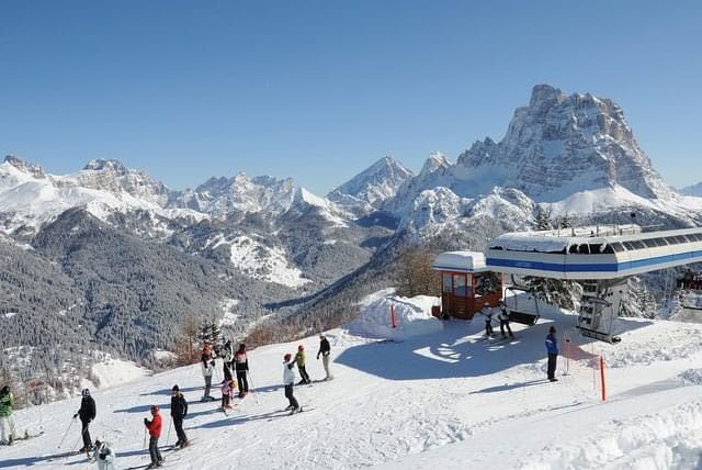 Immagine di un parco sci con ski lift e persone che praticano sci tra le montagne innevate e cielo sereno. Perfetto per articoli su attività invernali, sci, e turismo montano, ottimizzato per parole chiave legate al turismo invernale.