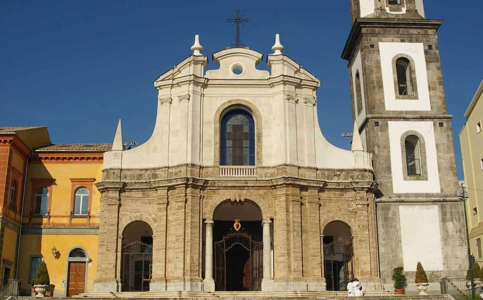 Elegante chiesa barocca con facciata in pietra e torre campanaria, situata in un contesto urbano con edifici colorati e un cielo sereno.