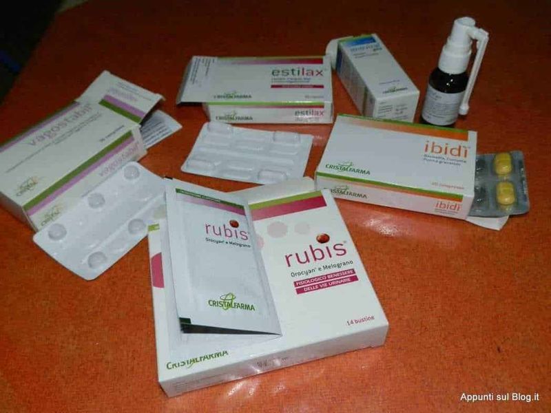 Farmaci e integratori per il tratto urinario, tra cui Ruby's e Estilax, dispersi su un tavolo di legno, con scatole, blister e spray spray.