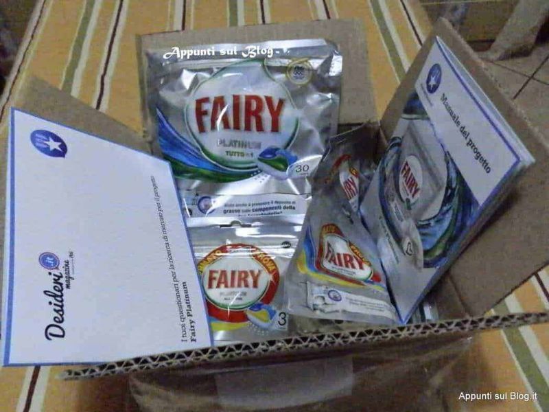 Polveri di detergente Fairy in confezioni multiple, all’interno di una scatola di cartone, pronti per l’uso, ambientazione domestica con tovaglia a righe.