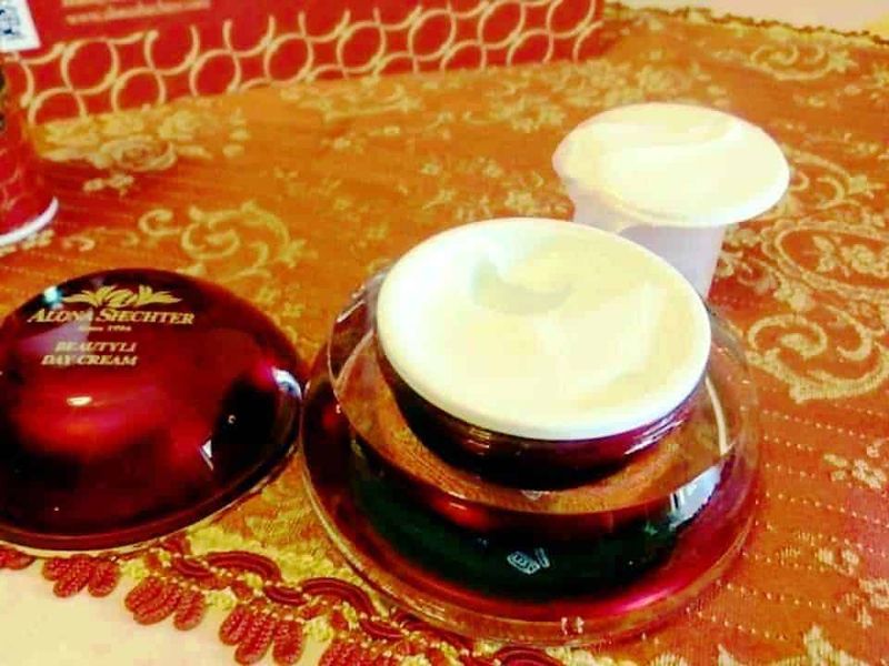 Crema viso alla calendula in barattolo con tappo di metallo, contenitore con crema bianca, sfondo tessuto rosso e oro, immagine di prodotti skincare naturali e bellezza, ripresa in ambiente domestico.