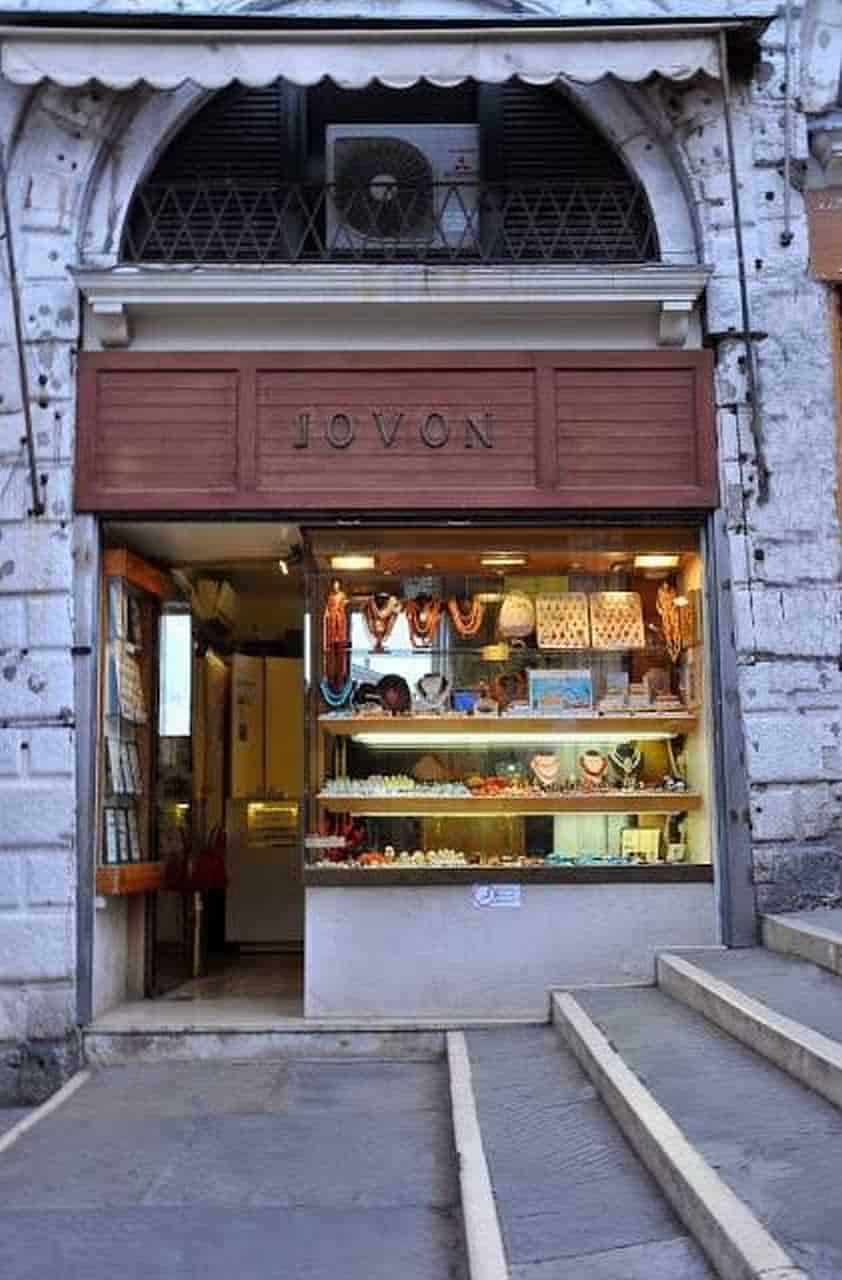 Vetrina di gioielli artigianali in un negozio storico di Roma, con esposizione di collane e orecchini colorati. Un piccolo negozio di gioielleria situato in un edificio antico con dettagli in pietra e un'entrata accogliente.