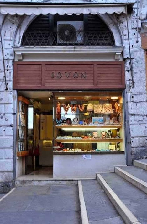 Eredi Jovon, gioielleria a Venezia dal 1934 2 Vetrina di gioielli artigianali in un negozio storico di Roma, con esposizione di collane e orecchini colorati. Un piccolo negozio di gioielleria situato in un edificio antico con dettagli in pietra e un'entrata accogliente.