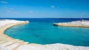 Lago di acqua cristallina tra scogli bianchi con cielo azzurro e mare calmo.