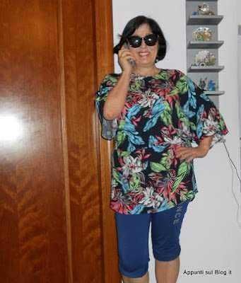 Telefono donna sorridente in casa, stile casual, abbigliamento floreale, accessori di occhiali da sole, atmosfera rilassata e amichevole.
