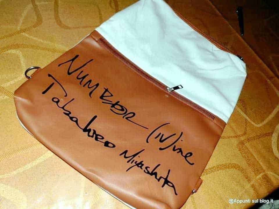 Borsa multifunzione 2 in 1 zaino e tracolla: Zaino con scritta "Nuntz (W)Vive - Tabacchio Mucashira" in caratteri neri su sfondo marrone e bianco.