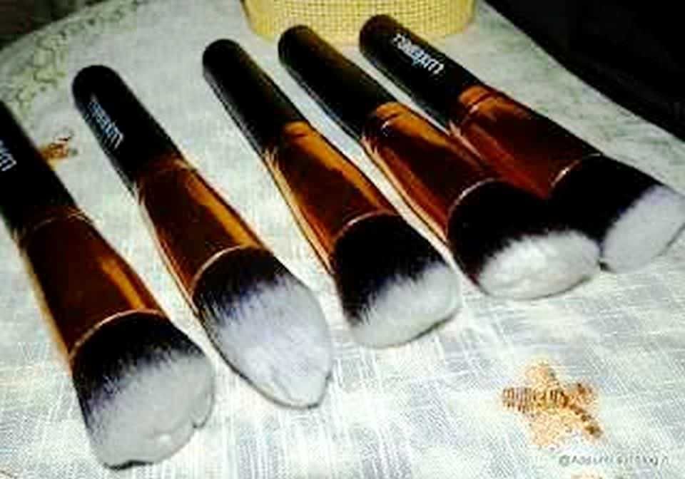 Pennelli di trucco professionali con manico nero e setole bianche, disposti su una tovaglia chiara, ideali per il make-up e la cura del viso, perfetti per ogni beauty artist.