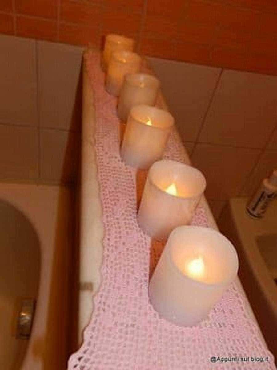 Candele accese su una mensola decorativa con tovaglia a maglia rosa, creando un'atmosfera calda e accogliente in un ambiente domestico.