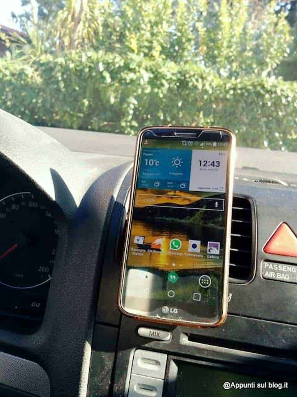 Smartphone appoggiato sul supporto dell'auto con vista sulla strada e sulla natura circostante, esempio di tecnologia per auto e connettività, ideale per blog di tecnologia e recensioni di dispositivi mobili.