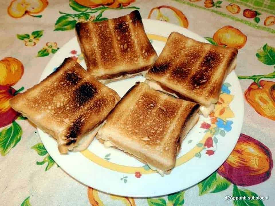 Pane imbottito tostato con formaggio, servito su piatto decorato con tovaglia a tema autunnale ricca di zucche e motivi colorati, perfetto per una merenda o colazione casalinga.