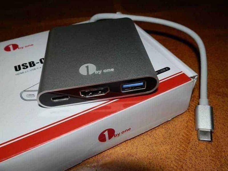 Adattatore usb 3.1 tipo c: Adattatore USB-C con porte HDMI e USB 3.0, collegato a un dispositivo elettronico nero con cavo bianco, su scatola bianca con logo rossa, ideale per connessione e trasferimento dati.