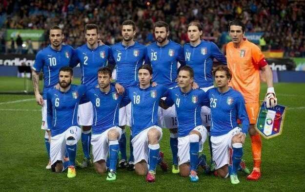 Ritratto della squadra di calcio italiana allineata sul campo prima di una partita, con divise azzurre e portiere in divisa arancione, in un evento sportivo internazionale.