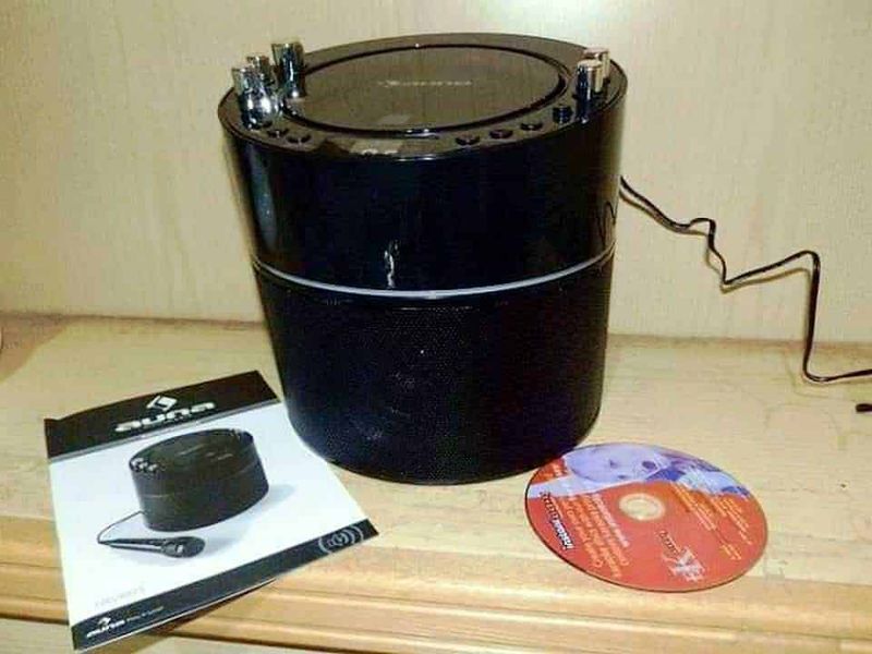 Alt text: Altoparlante wireless nero con cavo di alimentazione e manuale d'istruzioni, posizionato su superficie di legno.
