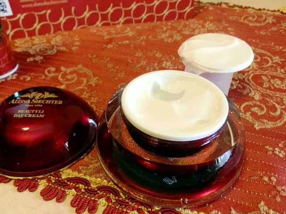 Crema viso naturale con ciotola, vaso e cappuccio bianco su tessuto arancione decorato, prodotti di bellezza artigianali, cura della pelle e benessere, cosmetici naturali.