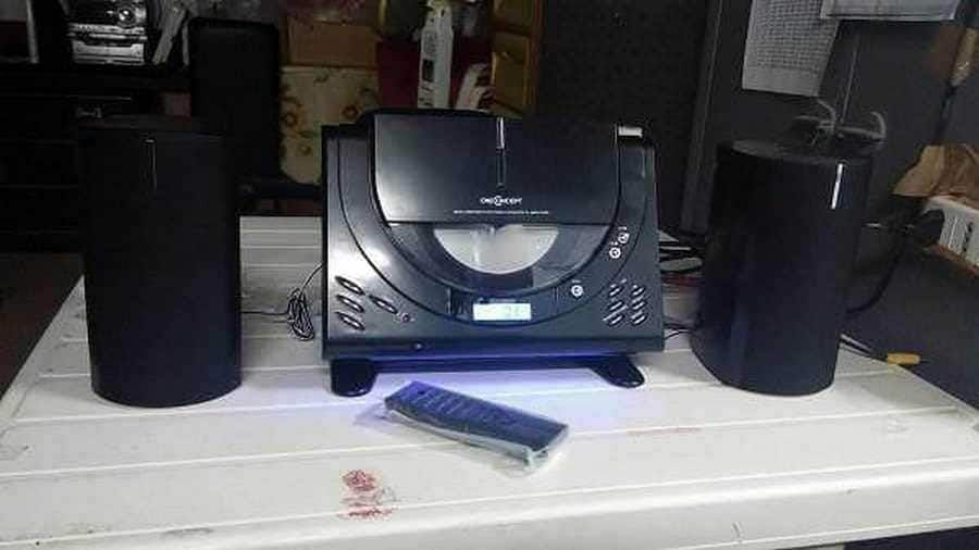 Alt text:Sistema stereo con lettore CD e due altoparlanti neri posizionati su un tavolo bianco, con telecomando davanti.