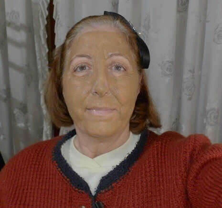 Canzoni di una donna anziana con capelli castani e trucco naturale, indossa un maglione rosso e sfondo di tende in tessuto.
