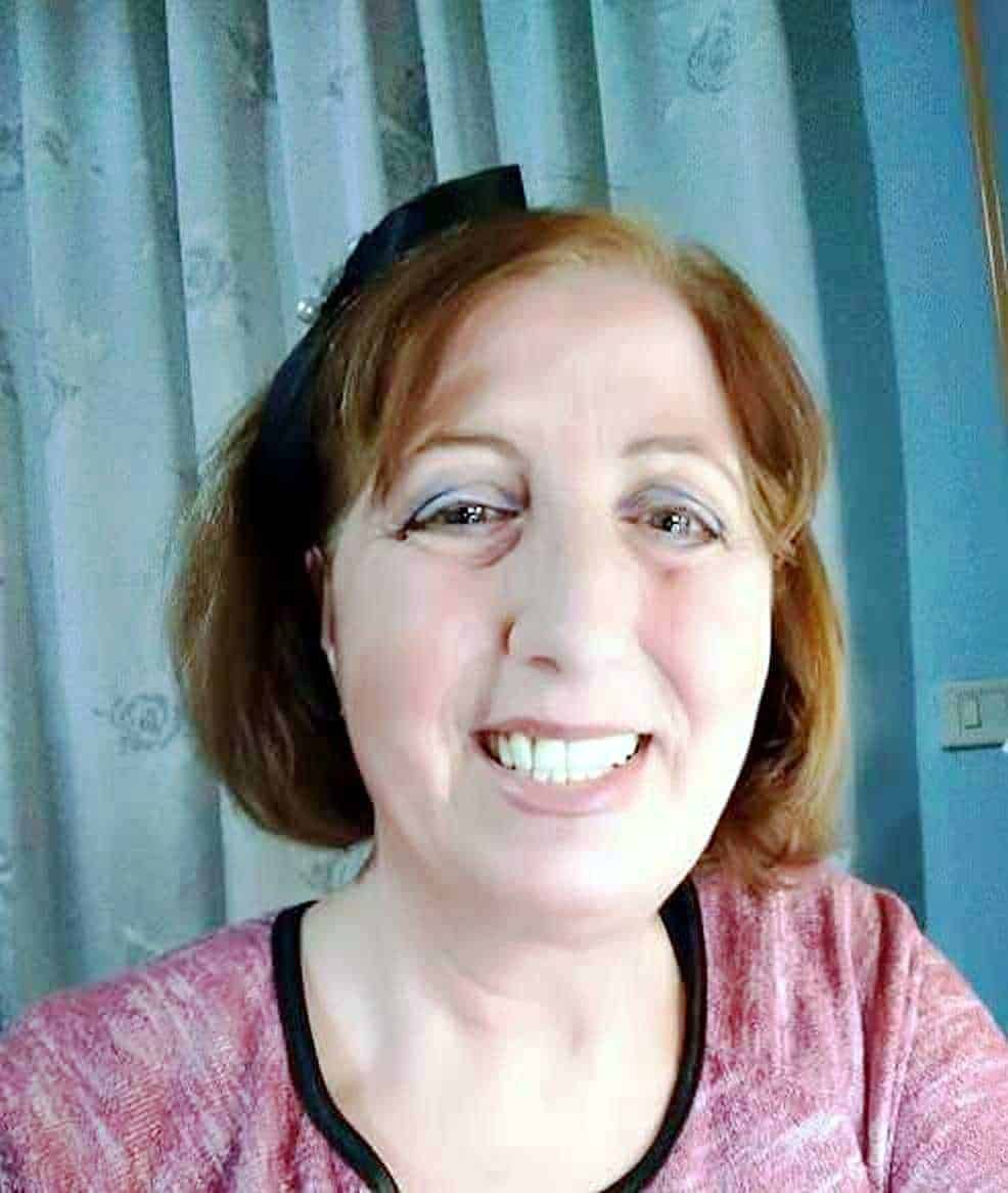 Ritratto di donna sorridente con capelli castano rossicci e camicetta rosa, sfondo tende di stoffa blu chiaro, ritratto di benessere e felicità, immagine positiva e accogliente per blog di lifestyle e benessere.