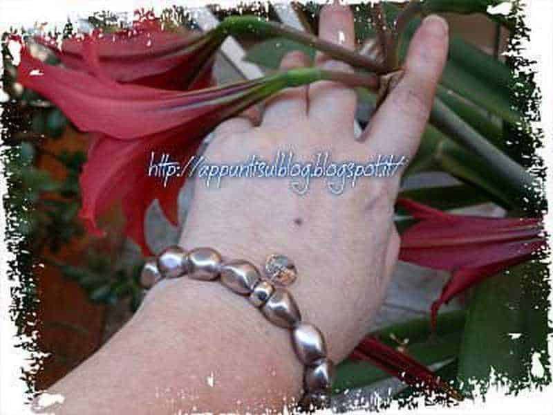 Berenice, gioielli inimitabili d'argento e perle oceaniche 4 Dahlia rosa con foglie verdi e petali eleganti, in primo piano con un braccialetto di perle argentate sulla mano. Ideale per immagini di fiori e giardinaggio, contenuti floreali, decorazioni naturali e bellezza floreale.