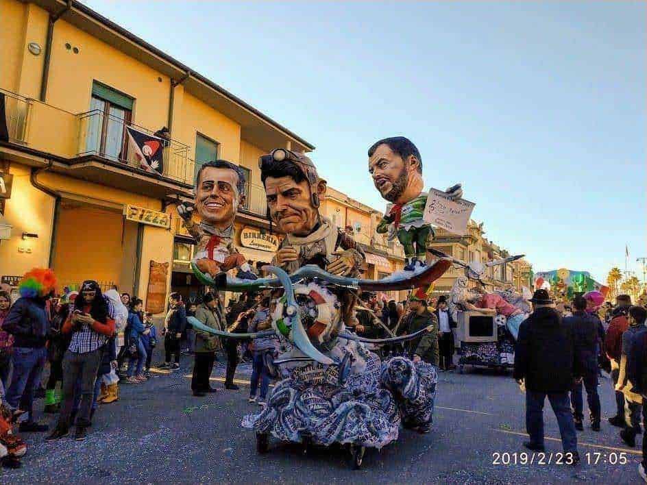 Carro allegorico con testine giganti durante una parata mascherata in strada in occasione di un carnevale, pubblico che osserva e partecipa alla festa, atmosfera vivace e colorata.