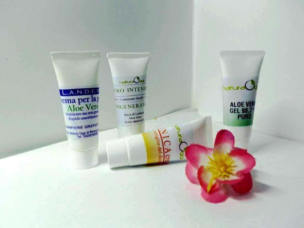 Creme per la pelle all'Aloe Vera e prodotti naturali per la cura della pelle, con fiore decorativo, su sfondo bianco, evidenziando la gamma di cosmetici naturali e idratanti.