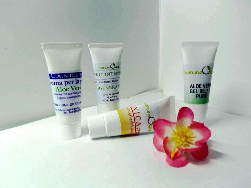 Cosmetici bio per rigenerare la pelle Natura Oggi 4 Creme per la pelle all'Aloe Vera e prodotti naturali per la cura della pelle, con fiore decorativo, su sfondo bianco, evidenziando la gamma di cosmetici naturali e idratanti.