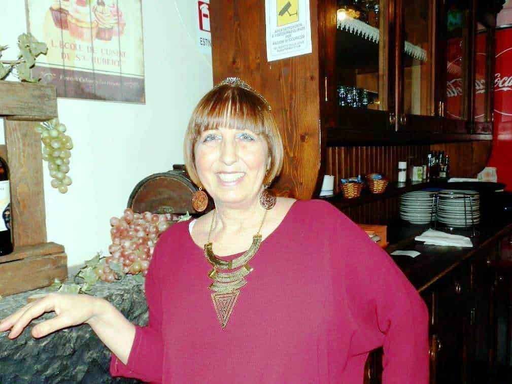 Viticoltrice sorridente in ristorante con decorazioni di uva e ambiente accogliente.