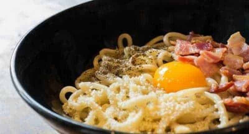 Uova, pancetta e formaggio sulla pasta in una ciotola nera, primo piatto tradizionale italiano.