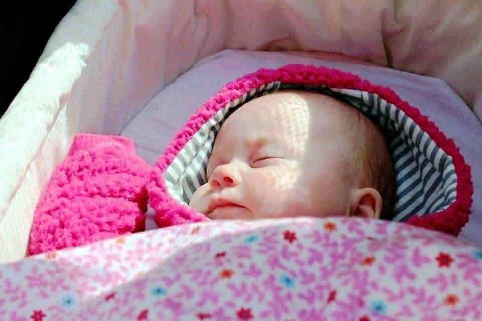 Bambino che dorme sotto una coperta rosa con cappuccio, immagini di tenerezza e tranquillità, ideale per articoli su neonati e cura dei bambini.