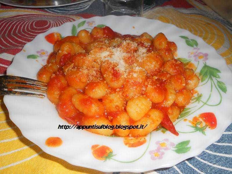 Deliziosi Gnocchi di Ricotta al Pomodoro con Parmigiano, piatto tradizionale italiano servito su piatto decorato con fiori, perfetto per una cena casalinga saporita e genuina.