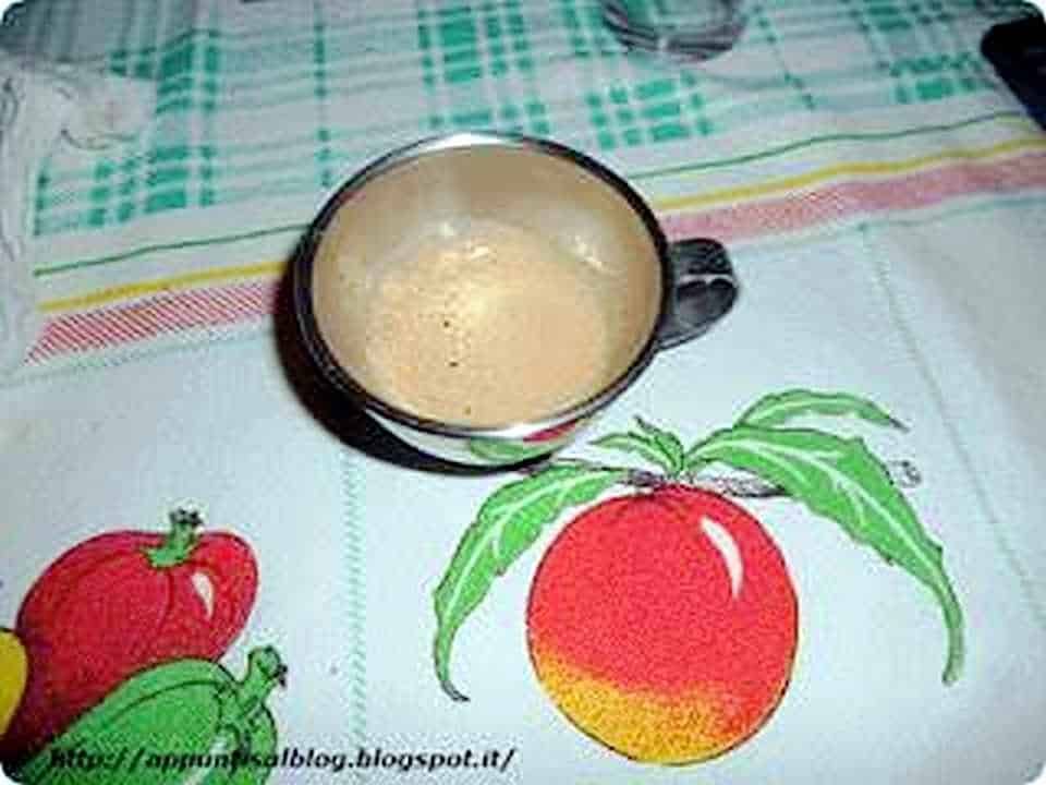 Tazza di caffè cremoso su tovaglia con frutta dipinta, atmosfera informale e accogliente, ideale per blog di ricette e lifestyle.