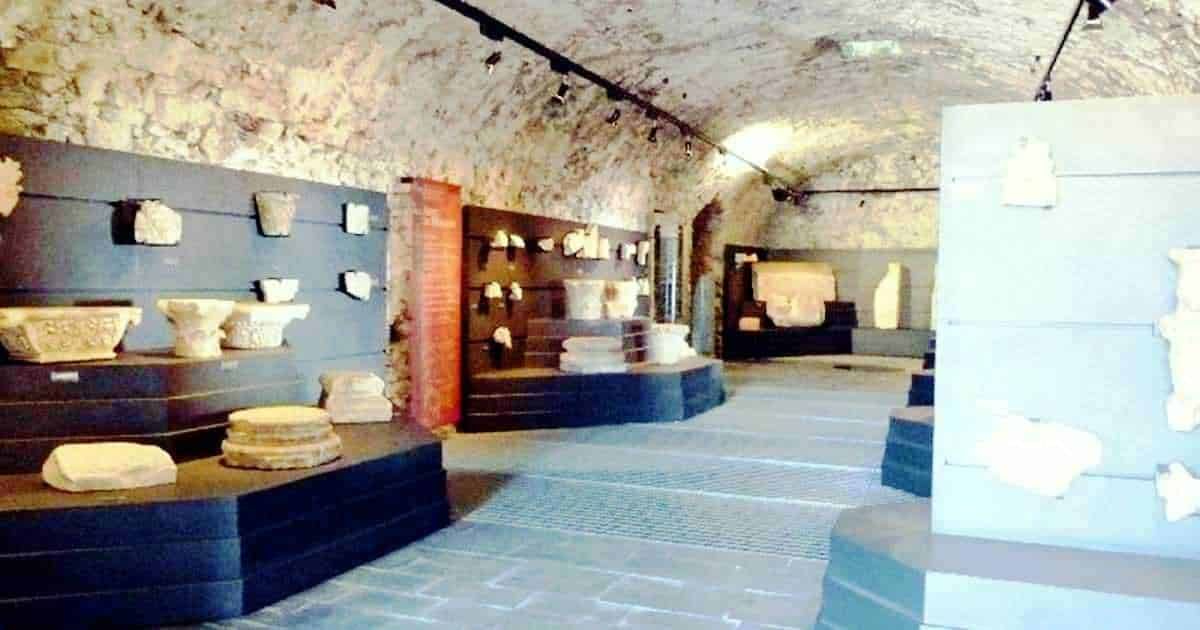 Antica Mostra di reperti archeologici in una galleria sotterranea, esposizione di ceramiche e manufatti storici, ambientazione unica con pareti in pietra e luci soffuse.