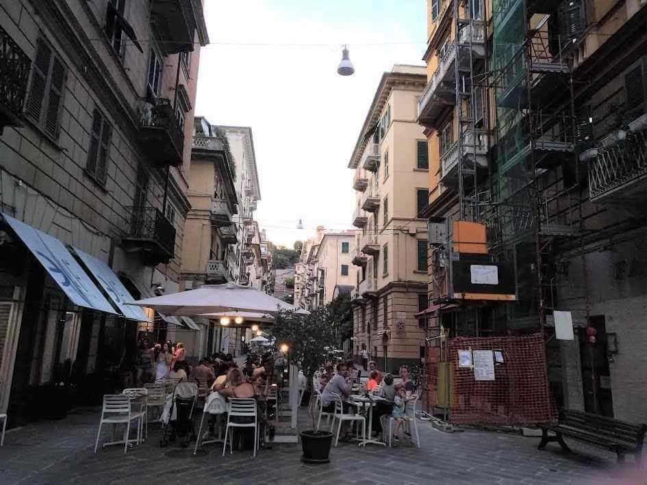 Vicolo suggestivo con tavoli all'aperto per rilassarsi e gustare cibo locale, circondato da edifici storici e lavoro di ristrutturazione, atmosfera autentica e vivace nel centro della città.