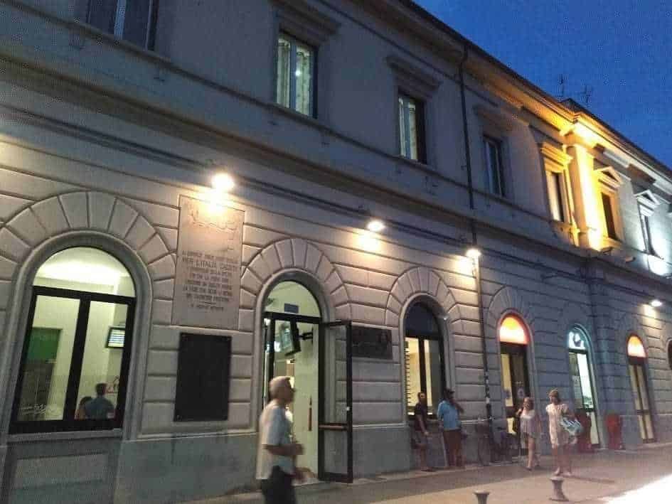Biblioteca storica illuminata di sera con persone in attesa all'ingresso, immagine di un edificio culturale a cielo aperto.