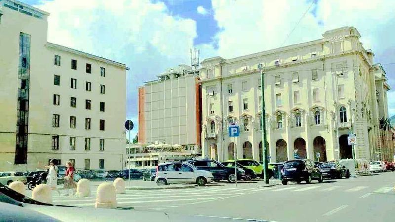 La Spezia siti d'interesse storici e moderni 2 Palazzi storici e moderni in centro città con parcheggio e traffico cittadino, vista artistica con cielo nuvoloso, immagine rappresentativa di un'area urbana affascinante.