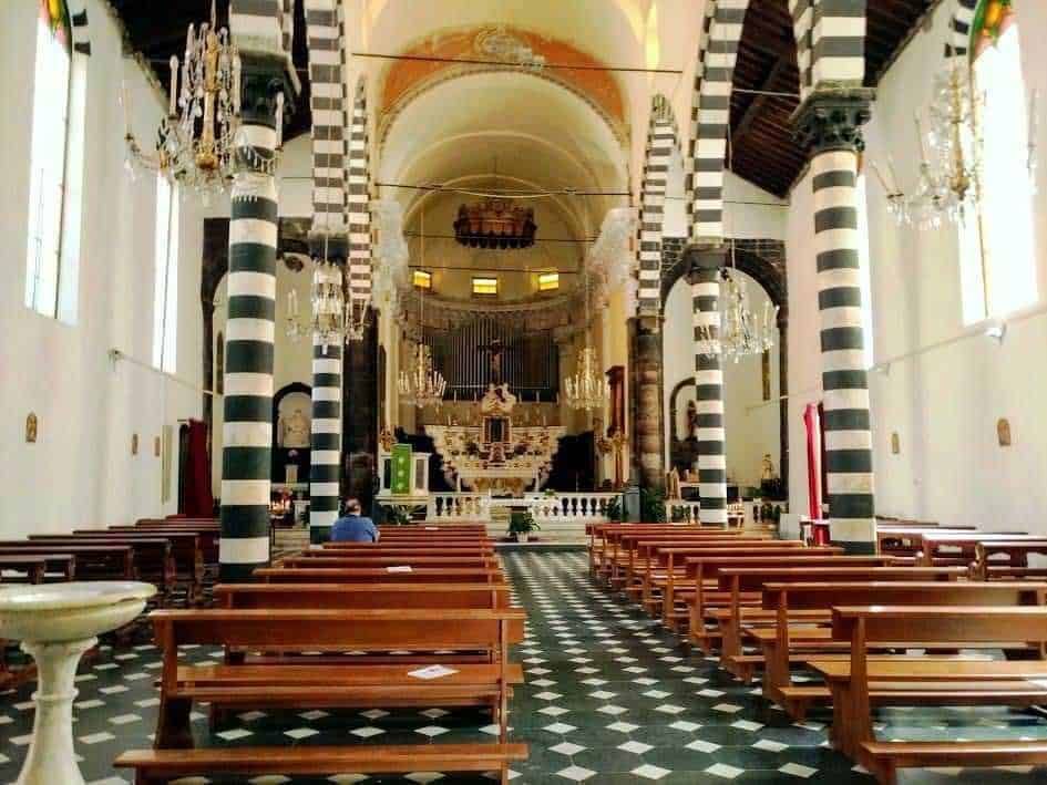 Interior chiesa storica con colonne a righe nere e bianche, candelabri in cristallo e arredi in legno, atmosfera sacra e suggestiva, ideale per turismo religioso e arte sacra.