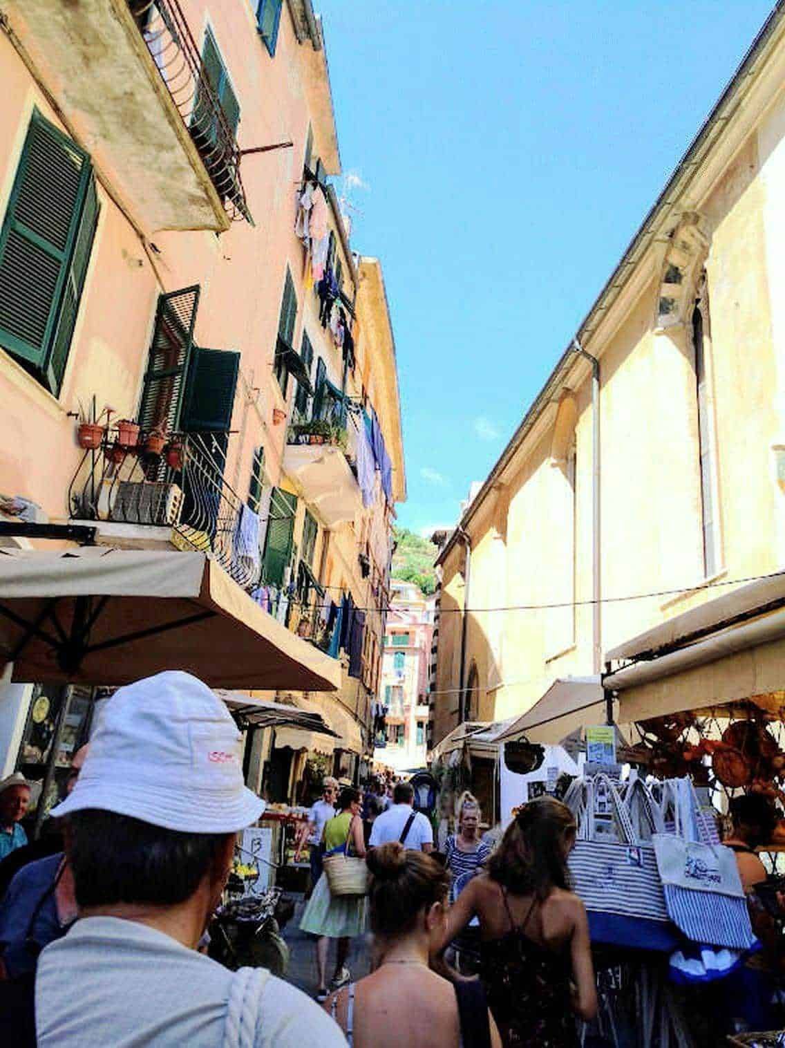 Colori vivaci di un mercato all'aperto nel centro storico di un'urbanistica italiana, con edifici colorati e persone che fanno shopping sotto il cielo azzurro.