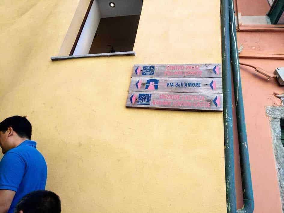 Appunti lungo le vie di un quartiere colorato, con segnali stradali in legno dipinti a mano, situati su una parete gialla di una città italiana vibrante e ricca di fascino locale.