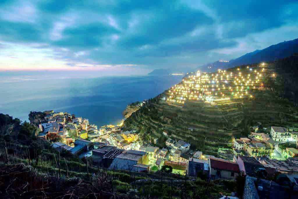 Vigneti terrazzati sul mare al tramonto, paesaggio costiero della costiera amalfitana, natura e abitazioni illuminate, vista panoramica sulla costa, atmosfera suggestiva e tranquilla.